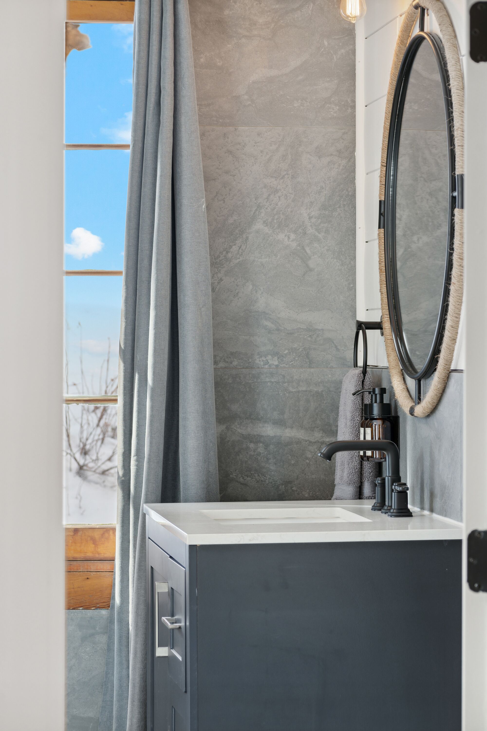 A bathroom with a stone wall, a mirror with a rope frame, a sink, and a towel rack.