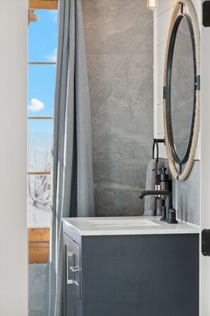 Une salle de bain avec un mur en pierre, un miroir encadré d’une corde, un lavabo et un porte-serviettes.