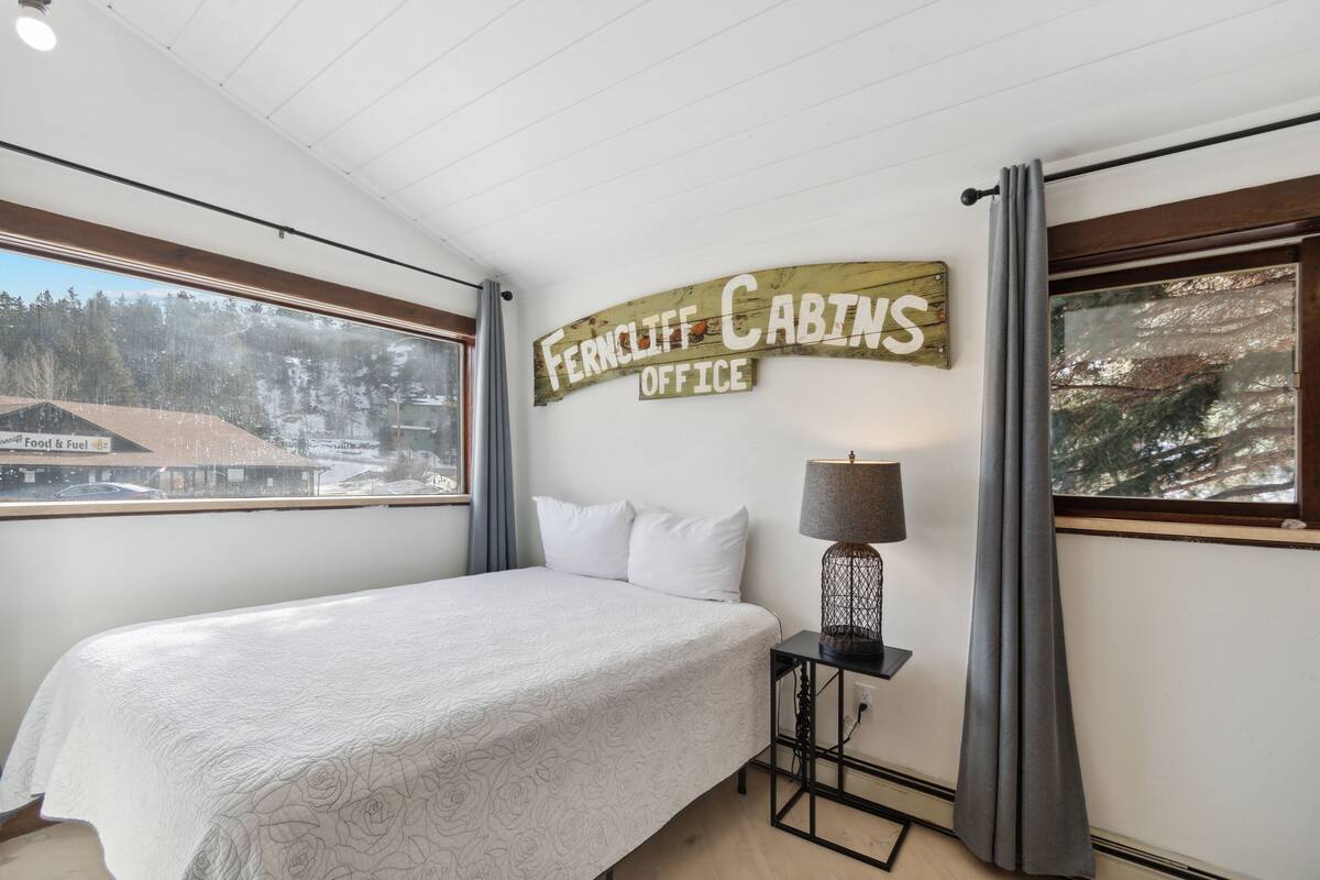 A bedroom with a bed, a nightstand, a lamp, and a sign reading "Ferncliff Cabins Office".