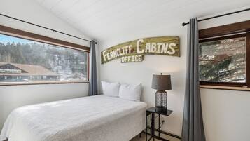 A bedroom with a bed, a nightstand, a lamp, and a sign reading "Ferncliff Cabins Office".