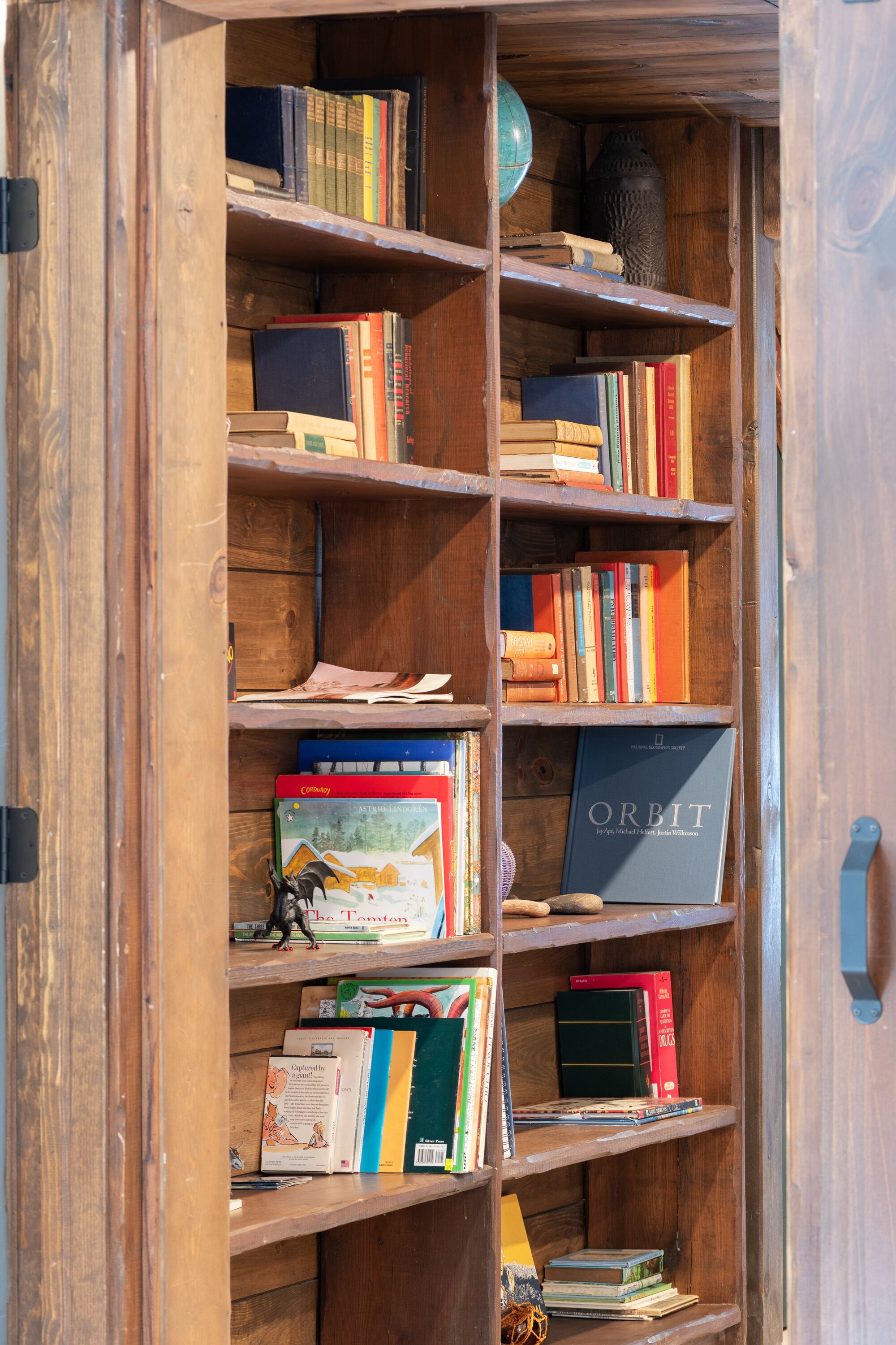 A wooden bookshelf filled with various books and a globe.
