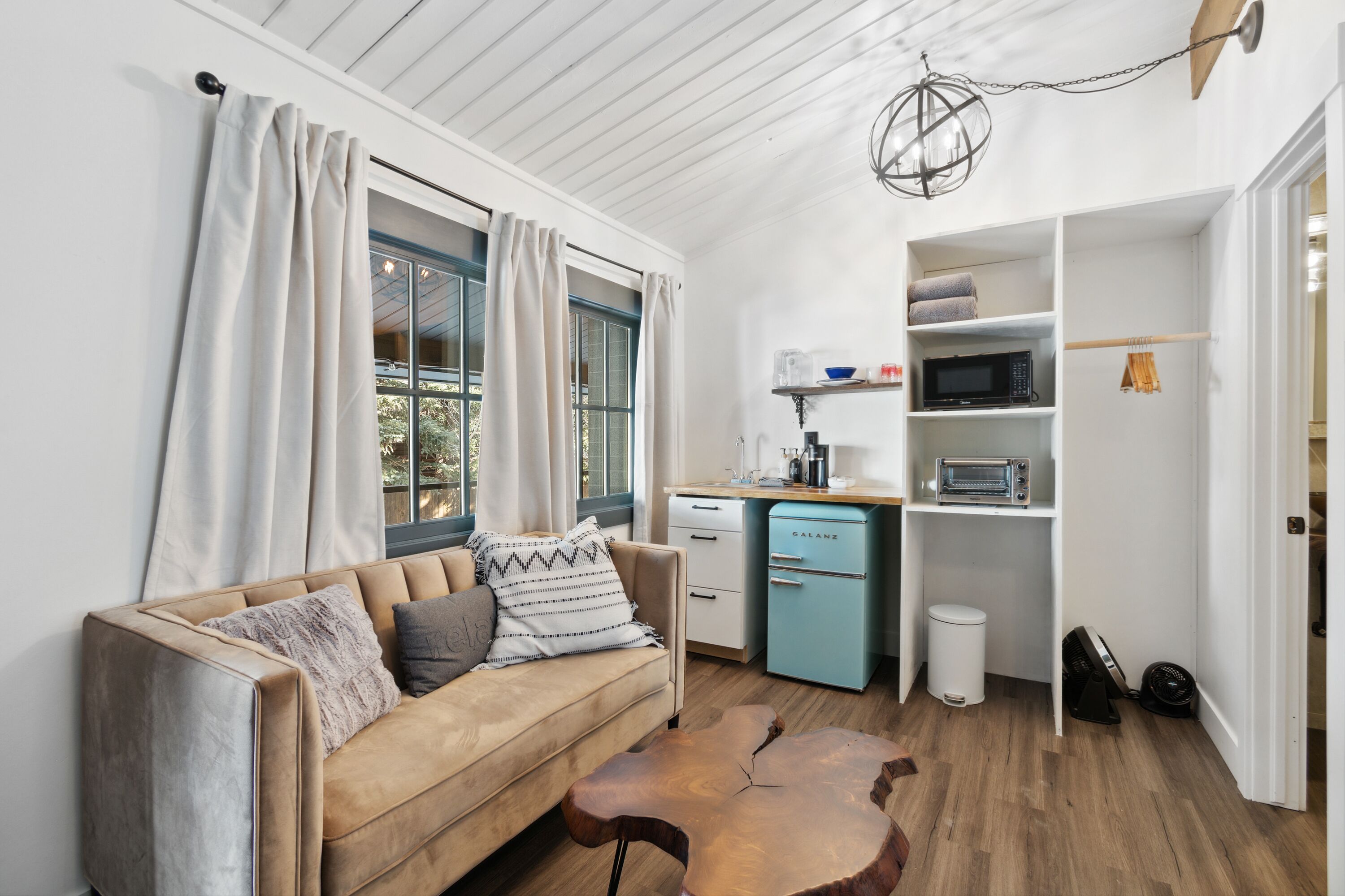 Un espace de vie compact comprenant un canapé, une table basse, une kitchenette équipée d’un four à micro-ondes et d’un grille-pain, ainsi qu’une petite poubelle.