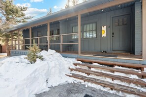 Une cabane dotée d’un porche abrité, d’un escalier en bois et d’un sol recouvert de neige.