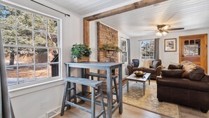 A cozy living room with a fireplace, a dining area with a table and chairs, and a large window offering a view of trees. - Ferncliff Lodge (Allenspark)