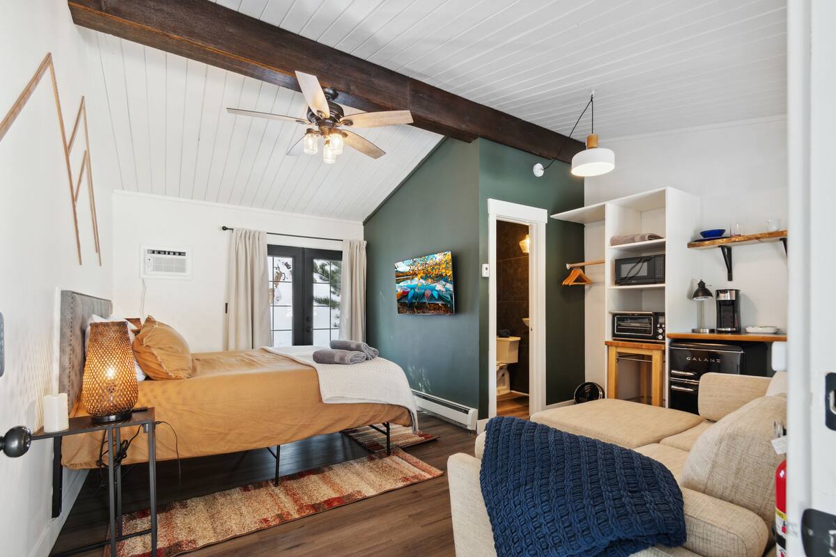 A modern bedroom with a bed, a sofa, a ceiling fan, and a TV.
