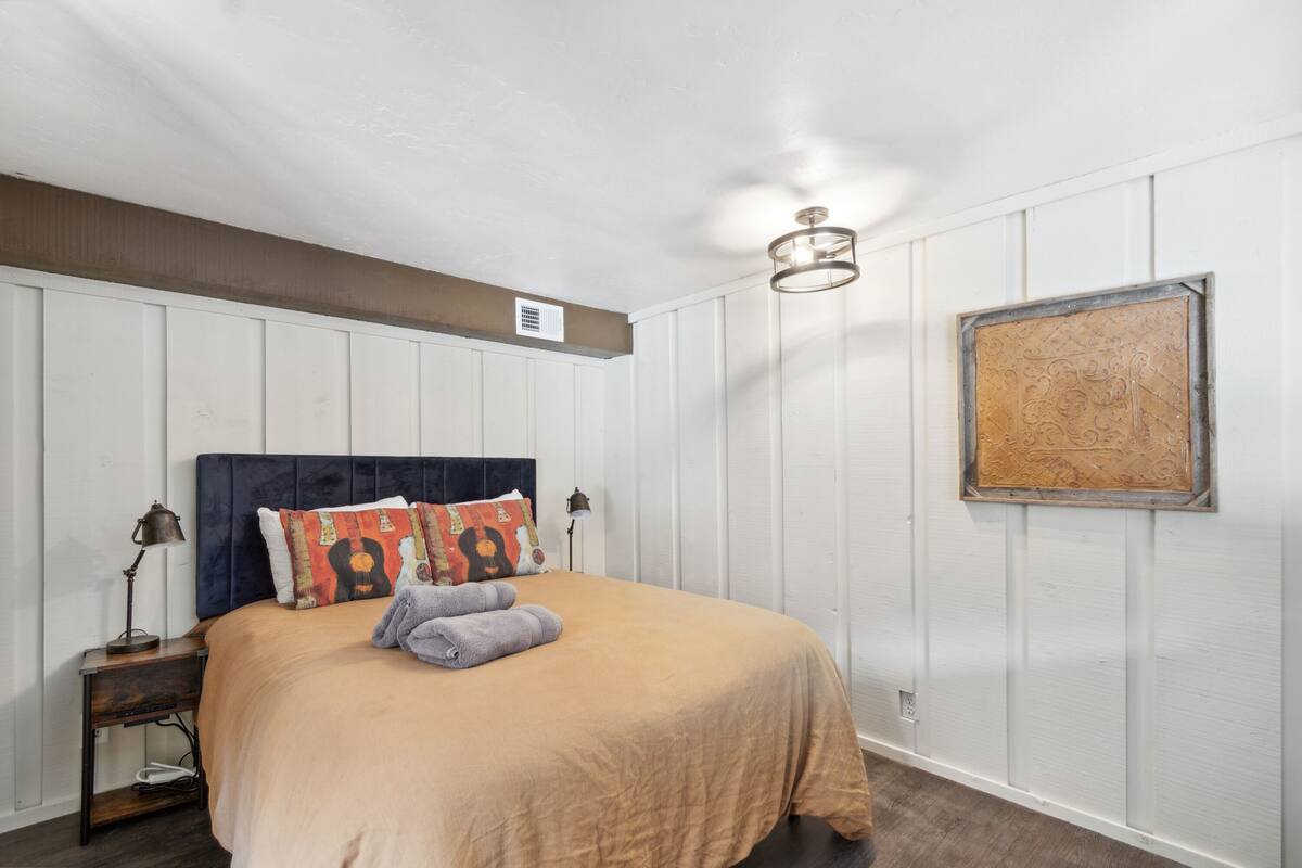 A neatly arranged bedroom with a bed, pillows, a nightstand, a wall-mounted light fixture, and a framed picture.