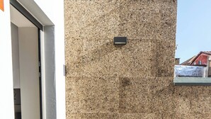 Um pequeno alpendre exterior com uma mesa de madeira e duas cadeiras, uma parede de pedra e um guarda-corpo de metal.