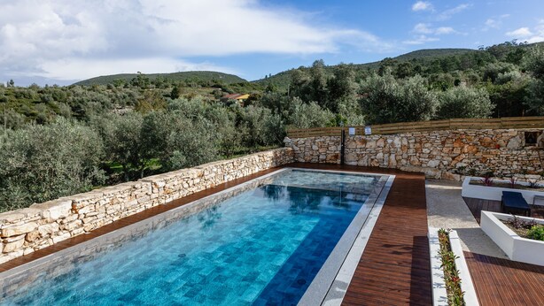 Una piscina rettangolare con pareti in pietra, circondata da un pontile in legno e un muro in pietra.