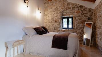 A bedroom with a stone wall, a bed with a headboard, a bedside table, a window, and a mirror.