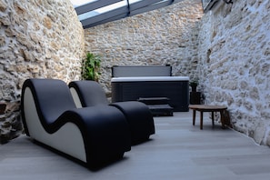 A modern outdoor seating area with a stone wall backdrop, a fireplace, and a wooden table. - Recantos d'Almerinda (Pombal)