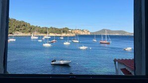 A coastal view with multiple boats anchored in calm waters, a clear sky, and a hilly landscape in the background.