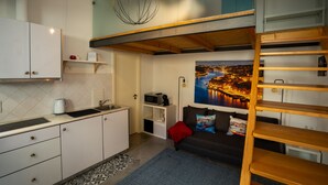 A compact kitchen with white cabinets, a microwave, and a kettle. There is a wooden loft bed with a view of a cityscape. - Ilha D’ouro House S. Vitor II (Porto)
