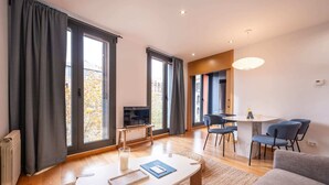 Un salon moderne avec un canapé, une table basse et un téléviseur. Il y a également un coin repas avec une table et des chaises.