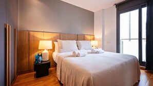 Une chambre d’hôtel moderne avec un grand lit, deux lampes de chevet, une tête de lit en bois et une grande fenêtre.
