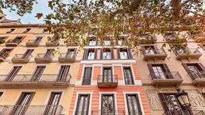 Un immeuble à plusieurs étages doté de balcons, une enseigne indiquant « Suites Center Barcelona », et un arbre aux feuilles d’automne au premier plan.