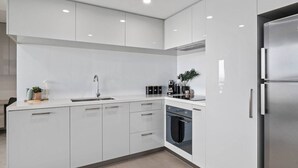 Une cuisine moderne avec des meubles blancs, un réfrigérateur en acier inoxydable et un four encastré.