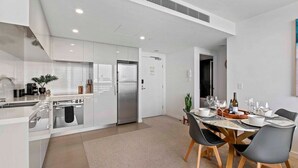 Une cuisine moderne avec des meubles blancs, un réfrigérateur en acier inoxydable et un coin repas avec une table dressée pour quatre personnes.