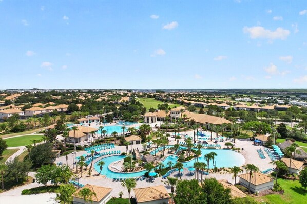A resort with multiple swimming pools, palm trees, and a view of the surrounding residential area.