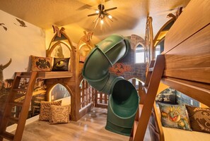 A room with a wooden playhouse, a green slide, and a ladder.