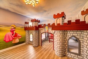A castle-themed playroom with brick walls, arched windows, and a mural of a princess on a mushroom.