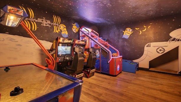 Quarto com jogos eletrônicos, piso de madeira e decoração com tema espacial.