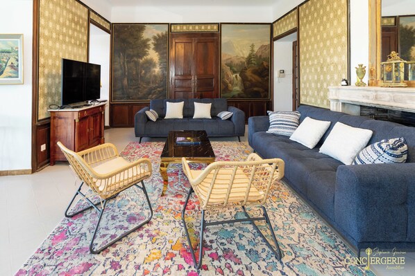 A living room with a sofa, two wicker chairs, a coffee table, a TV, and a fireplace. - Château d'Aiguèze (Aiguèze)