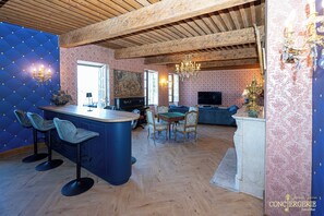 A spacious living area with a wooden ceiling, a bar with stools, a dining table with chairs, and a television. - Château d'Aiguèze (Aiguèze)