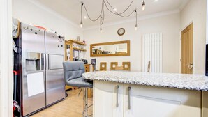 A modern kitchen with stainless steel appliances, a bar stool, and a wooden cabinet. - GuestReady - Tranquility near Shepherd's Bush (London)