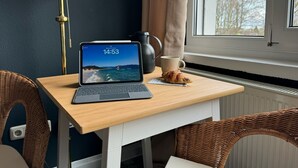 A laptop on a wooden table with a view of the sea, a coffee cup, and a croissant.
