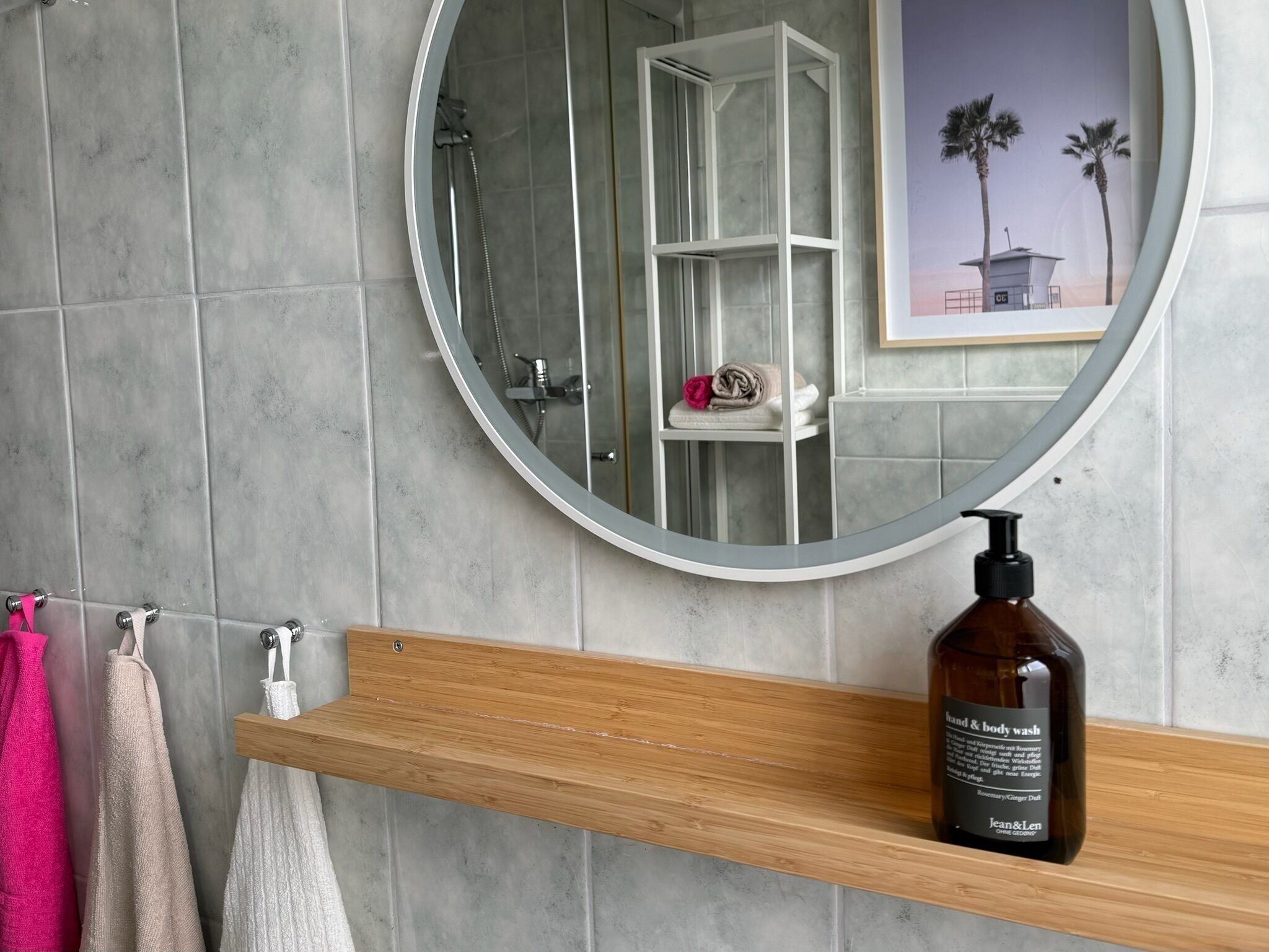 Ein Badezimmer mit einem runden Spiegel, einem Holzboden und einer Flasche Hand- und Körperseife.