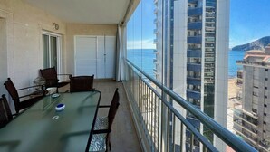 A balcony with a dining table and chairs, a white door, and a view of the ocean and buildings. - Alq 119 Porto Azul 12 Apartment (Calpe)
