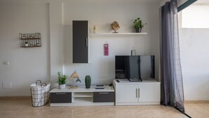 Una sala de estar moderna con un televisor de pantalla plana, un mueble blanco para equipo multimedia y una planta en maceta.