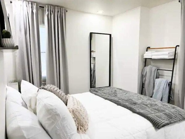 Un dormitorio moderno con cama, armario, espejo y perchero.