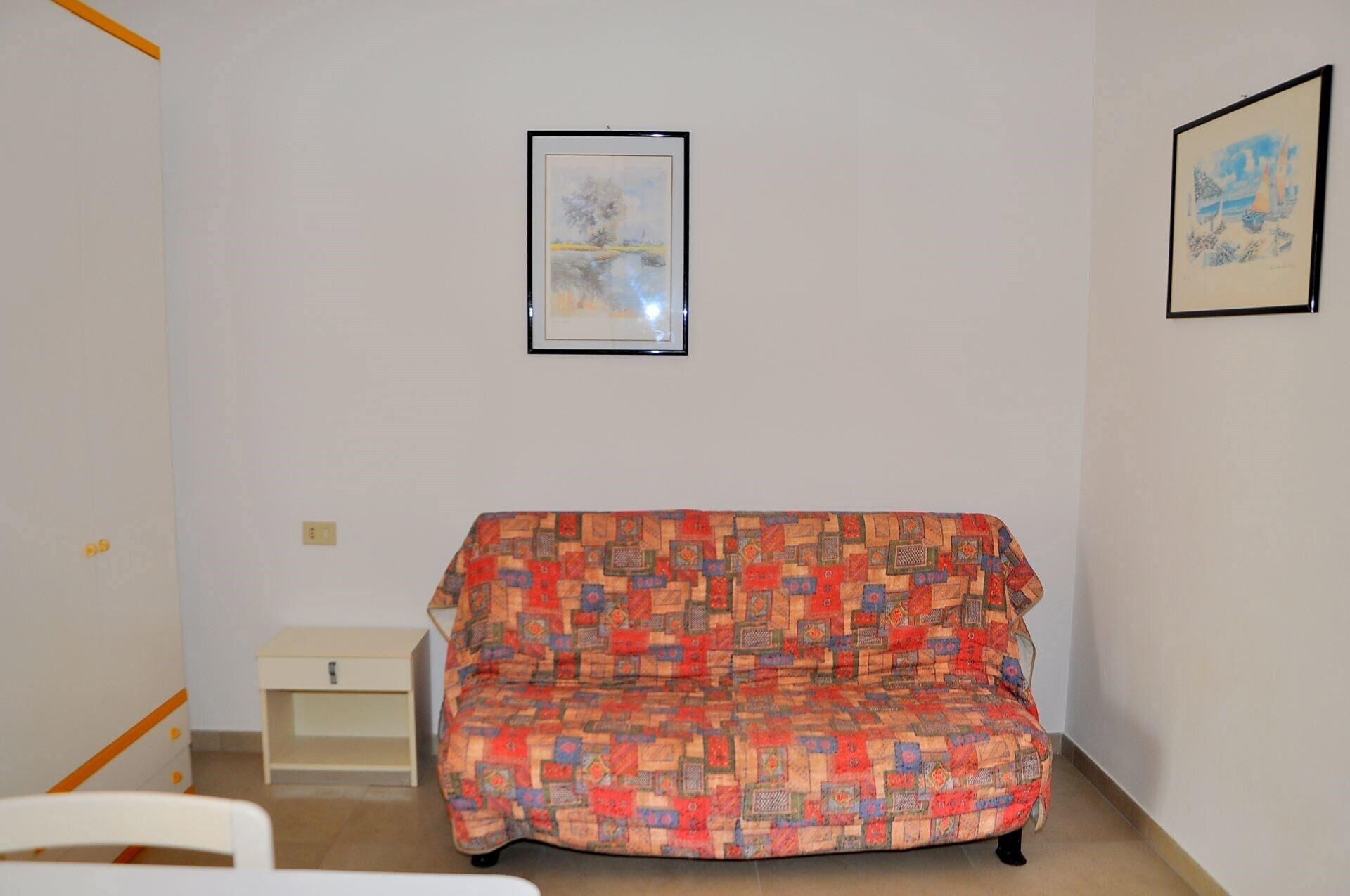 A room with a patterned sofa, a small white cabinet, and two framed pictures on the wall.