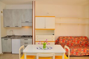 Cocina compacta con lavabo, cocina y armarios, una pequeña mesa de comedor con sillas y un sofá colorido.