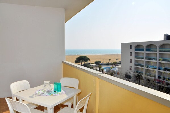 Ein Balkon mit Tisch und Stühlen, mit Blick auf einen Strand und ein Hotelgebäude.