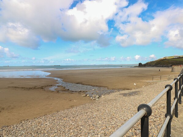 A beach with a pebble path leading to the water, a distant ship, and a rocky outcrop. - Coach House (Haverfordwest)