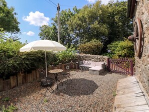A patio area with a table, chairs, a white umbrella, and a stone wall. - Coach House (Haverfordwest)
