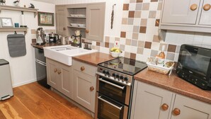 Una cocina moderna con estufa, horno y pileta de acero inoxidable. Hay armarios de madera y un salpicadero de azulejos.