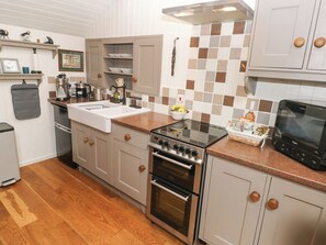 Eine moderne Küche mit Edelstahlkochfeld, -backofen und -spüle. Holzschränke und eine geflieste Spritzschutzleiste sind ebenfalls vorhanden.