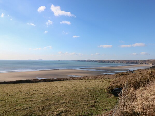 Eine Küstenlandschaft mit Strand, Wiesen und fernen Klippen unter blauem Himmel.