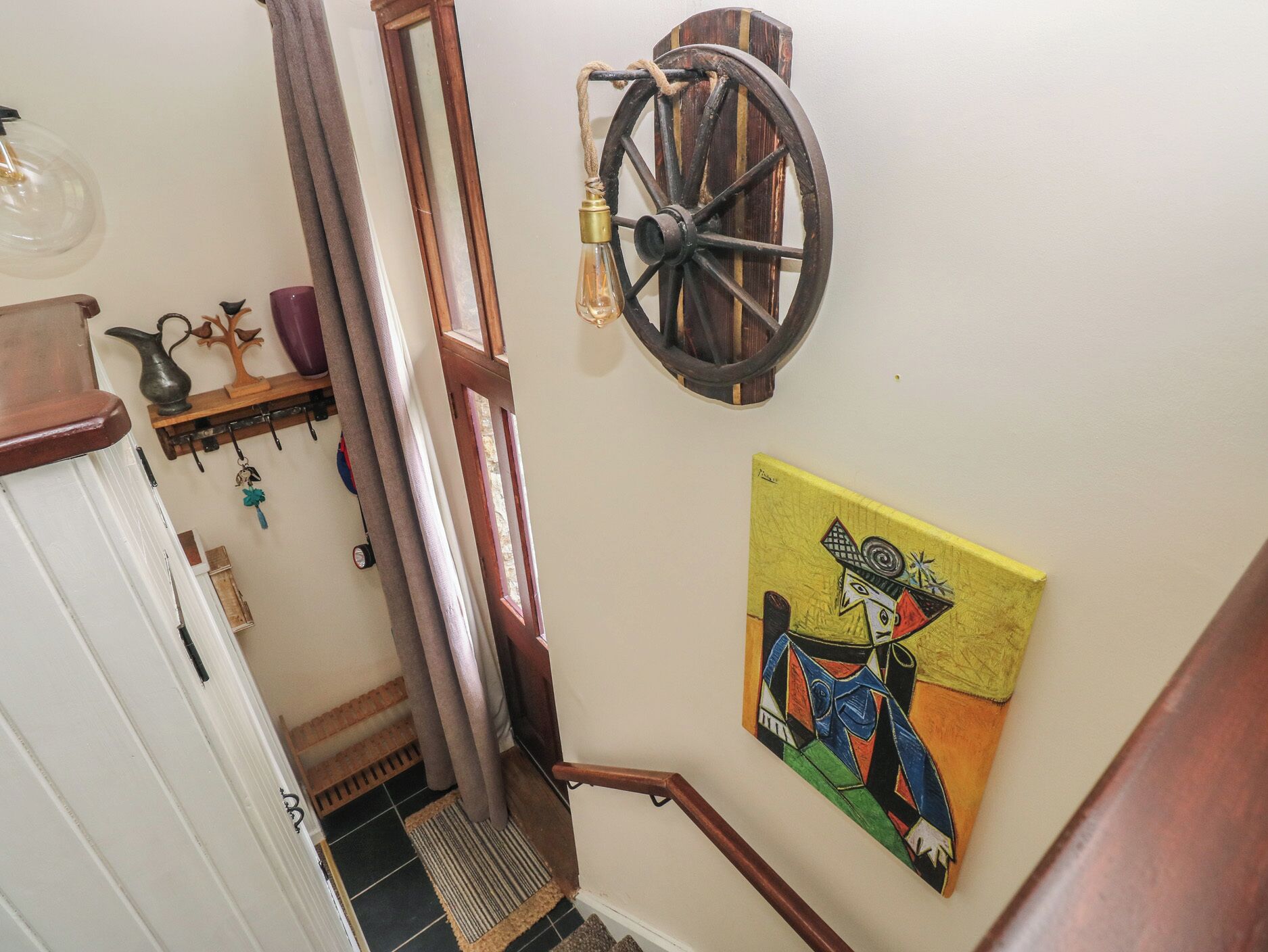 A staircase with a wooden handrail, a wall-mounted light fixture, and a colorful abstract painting.