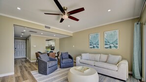 A spacious living room with a ceiling fan, a light-colored sofa, two armchairs, a round coffee table, and a rug. - Beautiful beachfront apartment on Seven Mile Beach! (George Town)