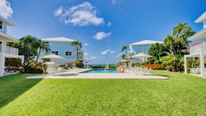 A pool area with a clear view of the ocean, surrounded by palm trees and modern buildings. - Beautiful beachfront apartment on Seven Mile Beach! (George Town)