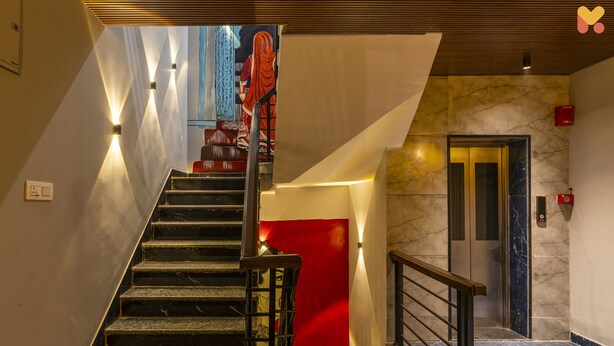 Un vestíbulo de hotel moderno con una escalera de mármol, una pared de acento roja y un ascensor.
