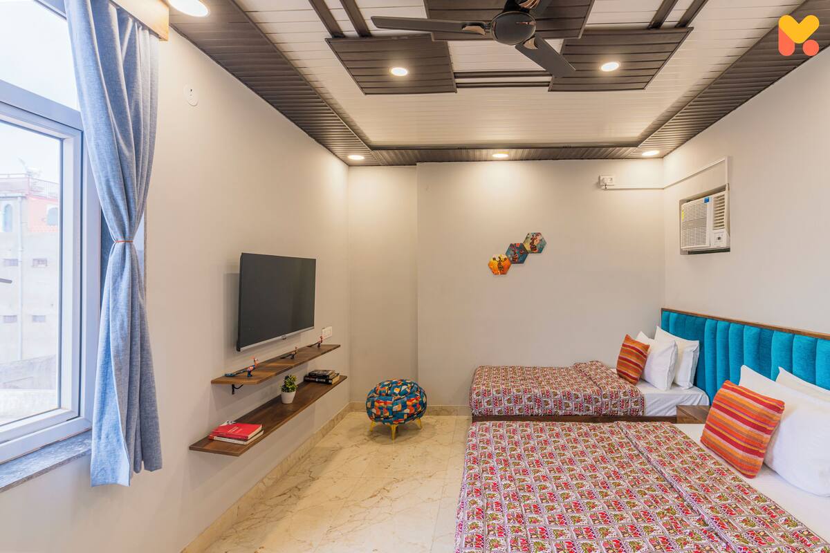 Une chambre d’hôtel avec deux lits, une télévision, un ventilateur de plafond et une fenêtre avec des rideaux.