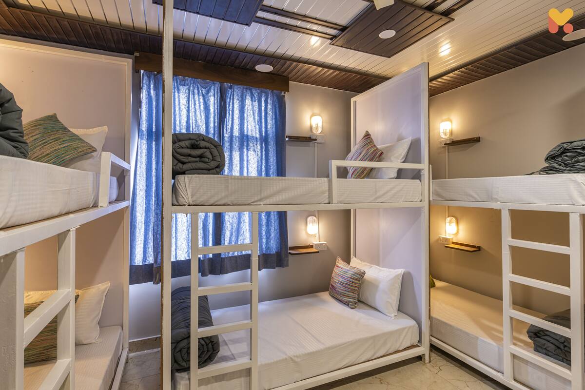 Une chambre avec un lit superposé, du linge de lit blanc, une échelle et des lampes fixées au mur.