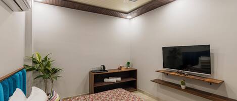 A bedroom with a bed, a TV, a ceiling fan, a plant, and a shelf with a TV stand.