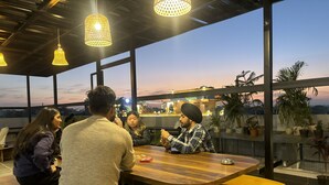 Un grupo de personas sentadas alrededor de una mesa de madera en un espacio interior moderno, bien iluminado, con ventanas amplias y plantas en macetas.