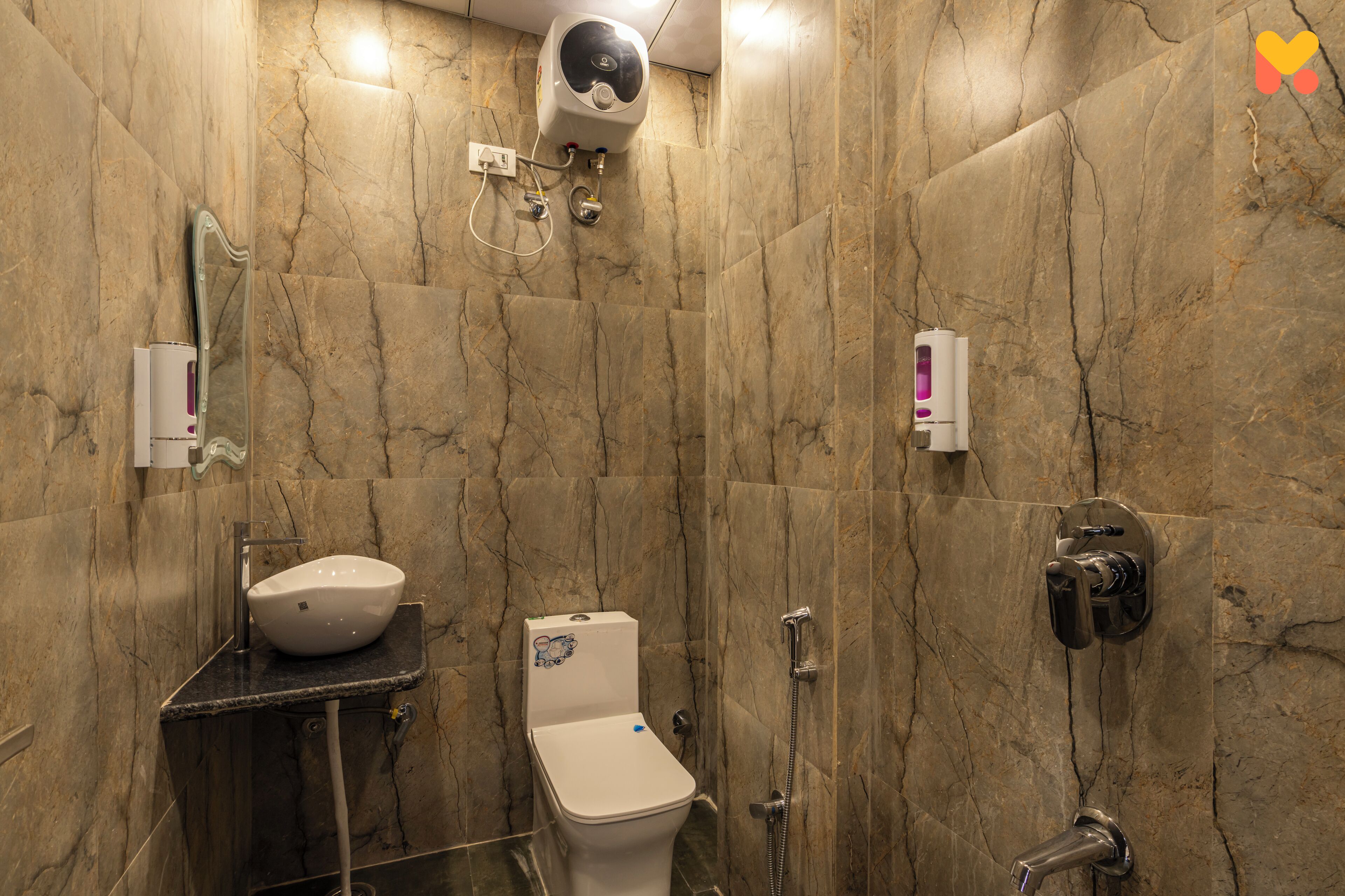 A bathroom with a marble wall, a sink, a toilet, a shower, and a hand dryer.
